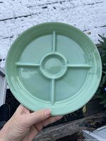 Front view of a jadeite green divided plate showing four compartments and a central round well, held outdoors with snow in background.