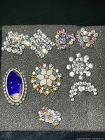 Top-down photo showing all pins and collar sets laid on black foam, highlighting rhinestone designs and the blue enamel pin.