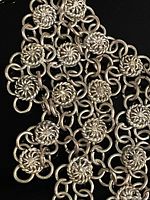 Close-up image showing intricate silver rings connecting small round facets with floral-like design on the necklace chain.