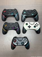 Set of 5 NS-L wireless gaming controllers in various colors on a grey surface.