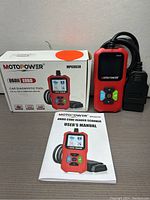 Photo of MOTOPOWER MP69038 OBDII code reader scanner with its box and user manual showing product image and model details.
