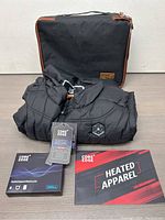 Core Edge heated vest folded and packaged with zippered carrying pouch, rechargeable battery pack box, and heated apparel booklet on a table.