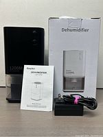 Photo showing the EasyAcc 1200ML portable dehumidifier alongside its user manual and power adapter, next to the original box.