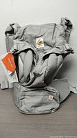 Front view of Ergobaby Omni 360 baby carrier in pearl grey showing brand labels, padded straps and zippered pocket on front waist belt.