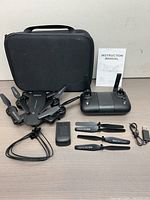 Foldable drone, remote controller, battery charger, extra propellers, carrying case, and instruction manual arranged on table.