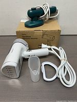 White handheld garment steamer with two nozzle attachments and power cord, shown with its original box.