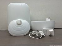 Disassembled humidifier parts showing main unit, detachable water tank, and power adapter on flat surface.