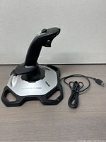 Full view of Logitech Extreme 3D Pro joystick showing the black and silver base with USB cable attached, joystick handle ergonomic with thumb buttons and trigger.