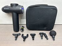 Photo showing Aerlang massage gun with six different attachments and black carrying case placed behind.