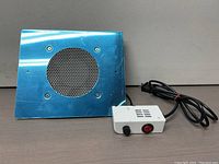 Photo of nail dust collector metal casing with circular perforated vent and control box with power switch, plugged in.