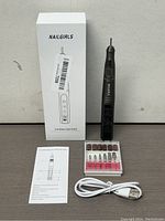 Full kit display including Nailgirls cordless nail drill, box, instruction manual, USB charging cable, and attachments case.