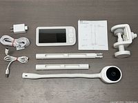 Complete set of the Netvue Peekababy A5 baby monitor showing handheld display, camera, adjustable clamp mount, power adapter, USB cables, and instruction manual on a dark surface.