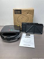 Ostera sandwich maker with two different cooking plates laid out alongside user manual and original box.
