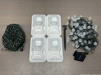 Set of various outdoor LED lights displayed on a table: coil of mini LED string lights, four rectangular LED spotlights, coil of globe LED string lights with solar panel and ground stake.