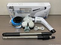 Electric spin scrubber with all brush heads, charging cable, and extendable handle poles in front of the product box.