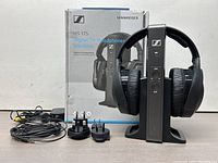 Sennheiser RS 175 wireless headphones system with transmitter and original box, power adapter with 3 different plug attachments, and audio cable arranged on white background.