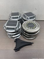 Top and side views of stacked solar dock lights with metallic silver housing and solar panels on top, accompanied by 4 black plastic stakes