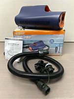Electric air pump on original product box with hose and nozzle adapters laid out on table.