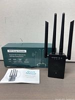 WiFi range extender device shown alongside original box and quick manual, all positioned against a neutral background.