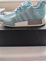 Side view of one Adidas NMD R1 sneaker showing knit upper, three stripes, Boost midsole with plugs, and Adidas branding