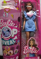 Photo showing Barbie Pop Reveal toy in original packaging next to Barbie doll in blue dress in packaging