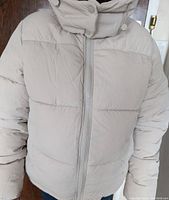 Front view of the beige women's bomber jacket zipped up, showing the padded quilting and high collar with snap button.