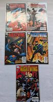 Five Nightwing comic books laid out on white surface, each in plastic protective sleeve, showing front covers with varied action scenes and different issue titles.