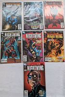 Photo shows seven Nightwing comic books arranged in two rows on a white surface, depicting various cover arts and titles, highlighting the condition and collection.