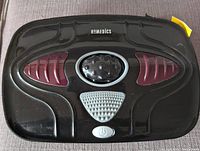 Top view of black Homedics foot massager with red pads and central gray textured area, power button visible.