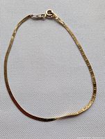 Full view of thin, flat 10k gold bracelet laid flat on light fabric background showing overall shape and clasp.