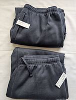 Two pairs of folded navy blue joggers showing tags, elastic waistband, and drawstrings.