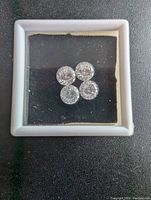 Top down view of all 4 loose round clear moissanite stones in box.