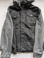 Front view of men's denim jacket with grey sleeves and attached hood
