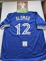 Full back view of blue Alomar #12 jersey laid flat with Sports Illustrated magazine above and PSA certificate below