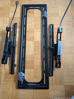 TV wall mount laid flat on floor showing main rectangular frame and two side arms for mounting and tilt function, screws taped to frame.