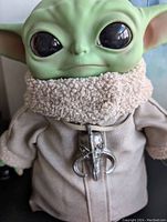 Close-up of the doll's face and upper chest showing large black eyes, green skin, and detailed soft fabric coat with a fluffy collar and a small toy blaster.