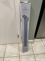 Photo of BabyBond baby gate in its original unopened box standing upright against a wall.