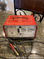 Red Motomaster car battery charger with front label showing 6 amp specification and attached charging clips lying on a countertop.