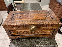 Top and front view showing intricate carved floral and geometric designs and brass clasp on chest lid.