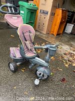 Side view of a Little Tykes push cart tricycle with purple padded seat and grey frame sitting on outdoor pavement.
