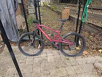 Side profile of purple full-suspension Raleigh mountain bike leaning against fence on paved patio