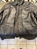 Brown leather men's jacket laid flat showing front, external pockets and collar snaps