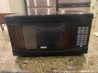 Front view of the black RCA microwave showing the keypad and door.