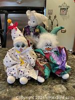 Front view of all three porcelain clown dolls seated next to each other on a table.