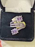 Front view of the sterling silver ring with pink square-cut gemstones surrounded by clear stones in a black velvet box.