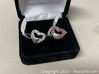 Two 925 sterling silver rings with heart designs in black and white cushioned jewelry boxes.