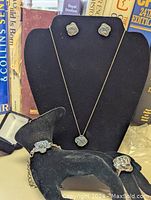 Full set displayed on black jewelry stands and holder, showing ring, bracelet, earrings, and necklace with pendant all featuring blue crystal rose designs