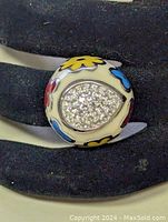 Front view of the stainless steel ring showing colorful enamel flower designs around a teardrop shaped cluster of cubic zirconia stones.