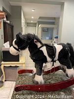 Side view of the black and white plush rocking horse on red rockers, showing mane, tail, saddle, and battery compartment.