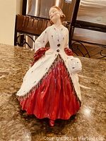 Front view of ceramic Royal Doulton figurine wearing white ermine coat with black spots and red dress, holding muff